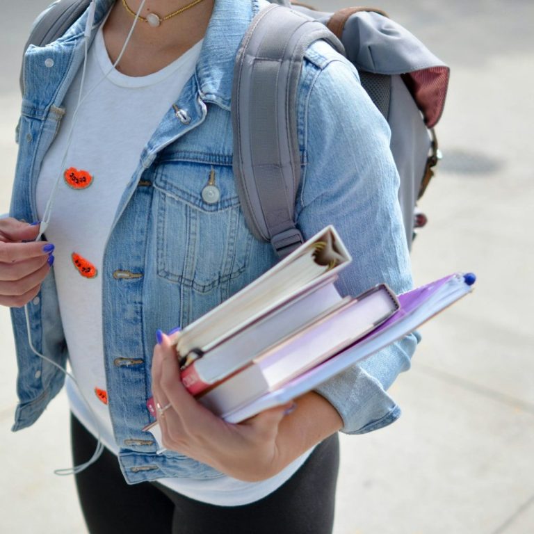 Metodología Persona con mochila que sostiene varios libros en una mano. Lleva una camiseta clara.